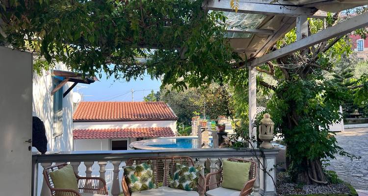 Coin salon confortable sous une pergola à côté d'une piscine.