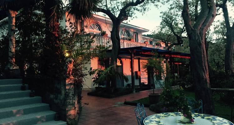 Vue du soir d'une villa avec des arbres et des sièges extérieurs.