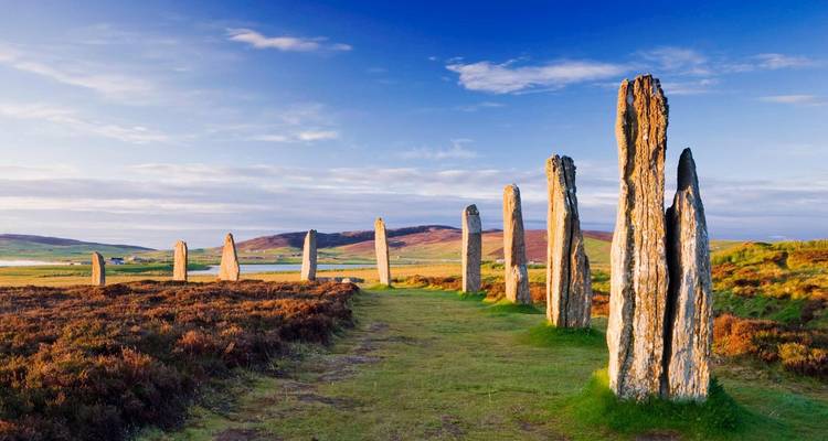 Tall, ancient standing stones at sunset in an open, green field.