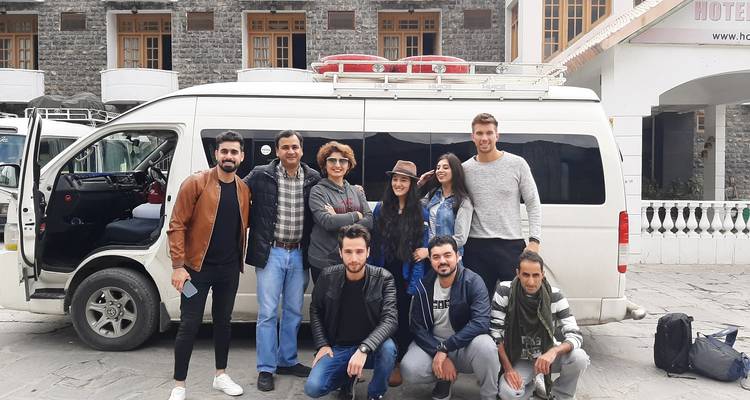 Groep reizigers poseert voor een busje geparkeerd voor een hotel.