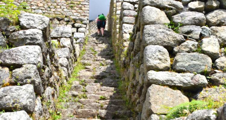 Een persoon die een smalle stenen trap beklimt, geflankeerd door rustieke muren.