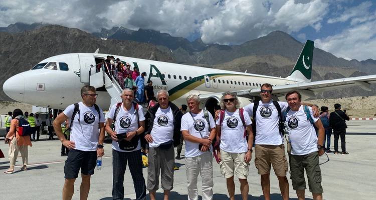 Groep mannen poserend voor vliegtuig met bergen