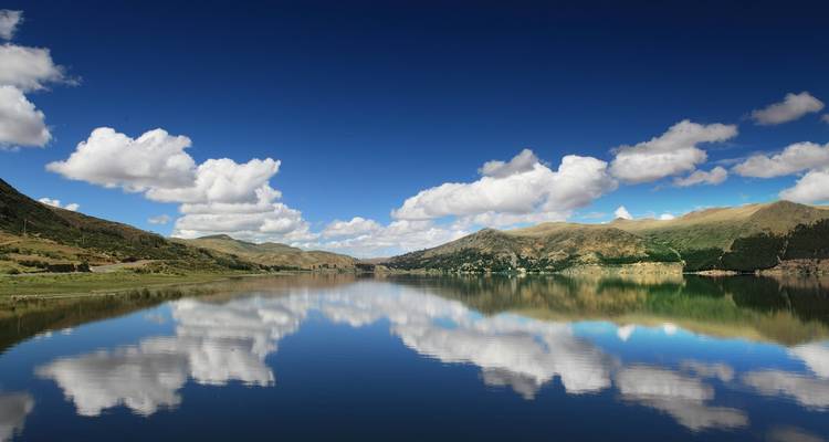 Sereen meer met bergen die reflecteren in het water onder een heldere blauwe hemel.