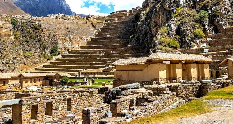 Stone terraces and structures in an archaeological site with mountains in the background.