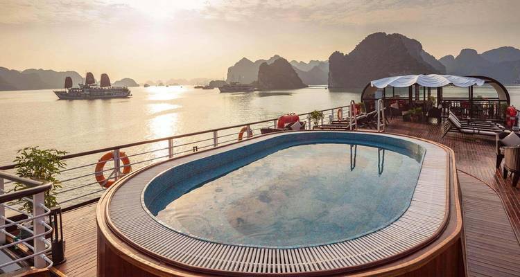 Lever de soleil sur une petite piscine ovale sur le pont d'une croisière avec les pics de la baie d'Ha Long en silhouette contre le ciel.