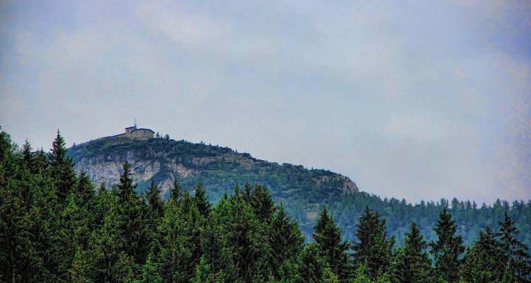 Vue lointaine d'une montagne avec une structure au sommet entourée d'arbres.