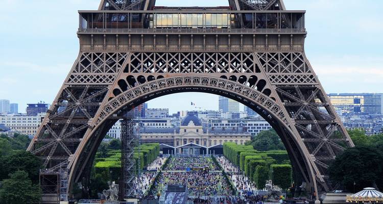 Blick auf den Eiffelturm mit einer großen Menschenansammlung darunter, umgeben von Bäumen und Gebäuden.