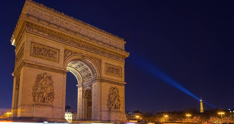 Verlichte Arc de Triomphe met een schijnwerper, tijdens de nacht.