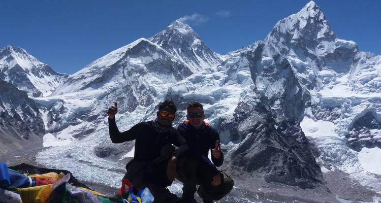 Two people posing in front of snow-capped mountains with clear blue skies.