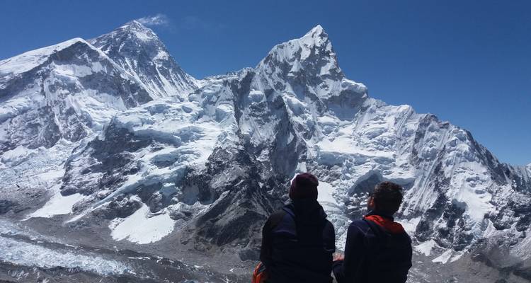 Two people sitting and observing snow-covered mountains.
