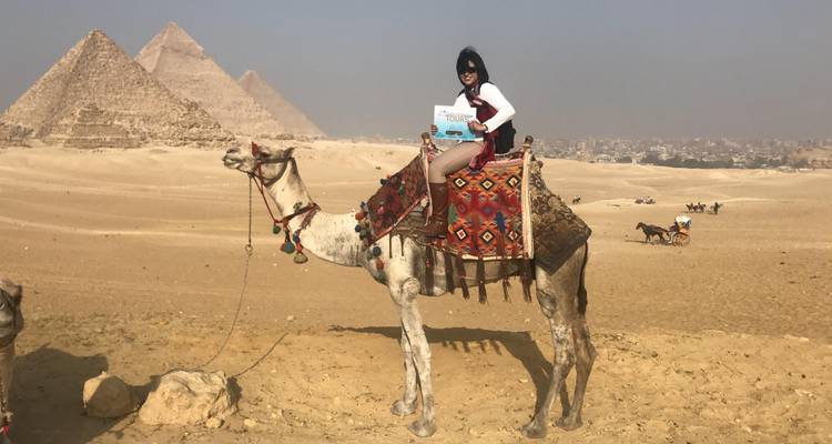 Persoon op een kameel met piramides op de achtergrond.