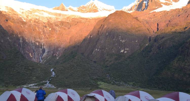 Campsite with tents and snow-capped mountains lit by the setting sun.