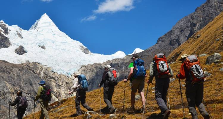 Group of hikers moving upwards towards a snowy peak.