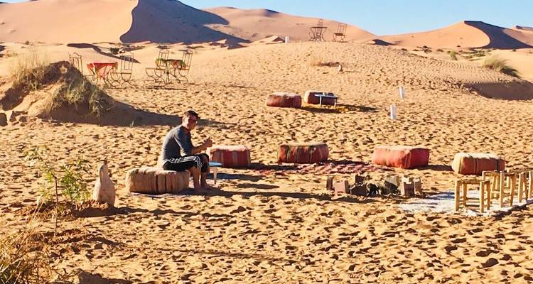 A man sitting on a sand dune surrounded by seating arrangements.
