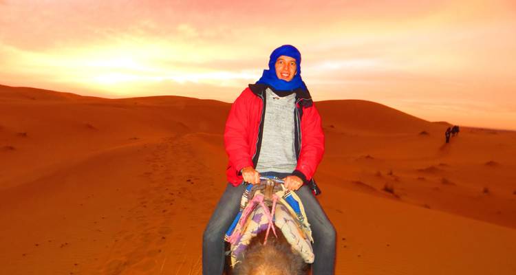 A man riding a camel during a colorful sunset in the desert.