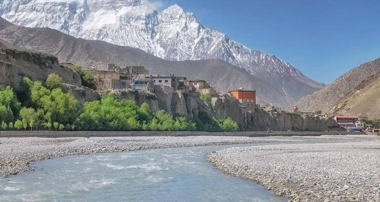 Une rivière qui coule près d'un village avec des montagnes en arrière-plan.