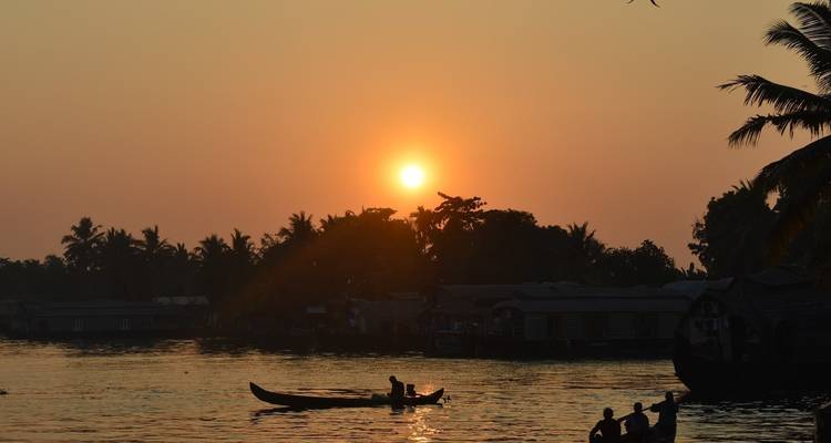 Sonnenuntergang über dem Wasser mit Silhouetten von Booten und Bäumen.