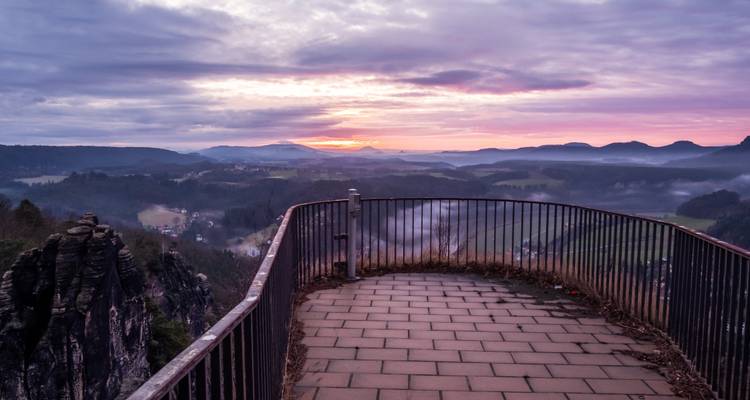 Une vue de coucher de soleil depuis un point d'observation clôturé surplombant une vallée.