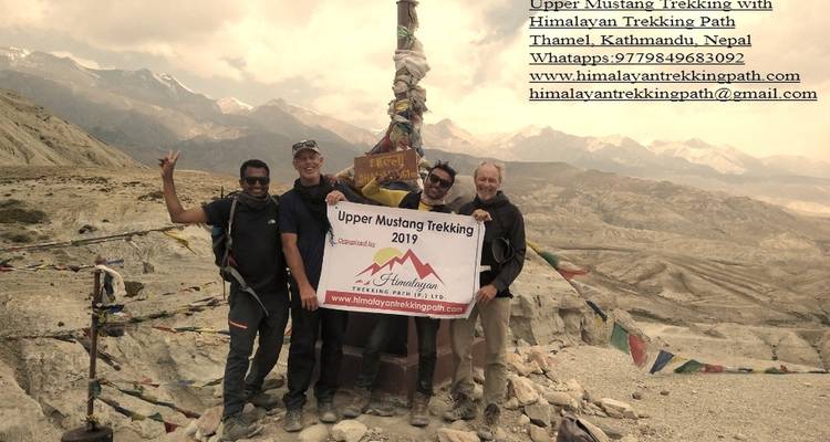 Gruppe von Menschen, die ein Wanderschild halten, mit Bergen im Hintergrund.