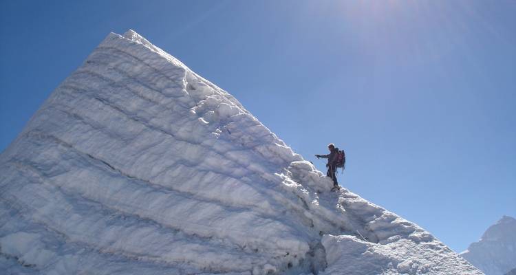 Bergsteiger auf einem verschneiten Grat bei blauem Himmel.