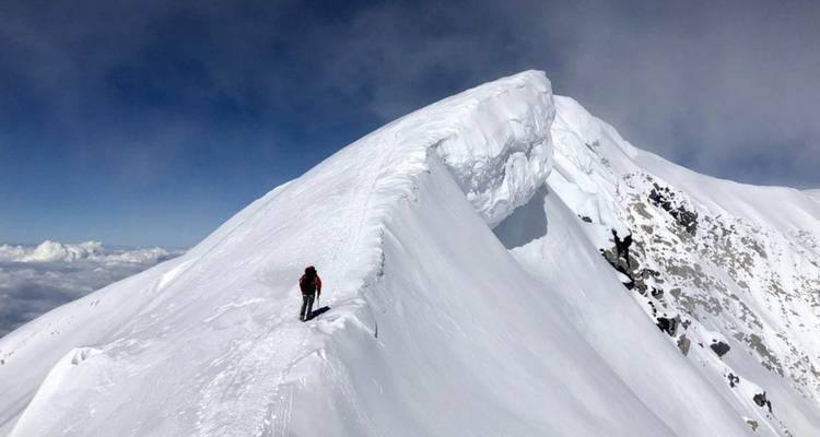 Einzelner Kletterer auf einem schneereichen, windgepeitschten Gipfel.