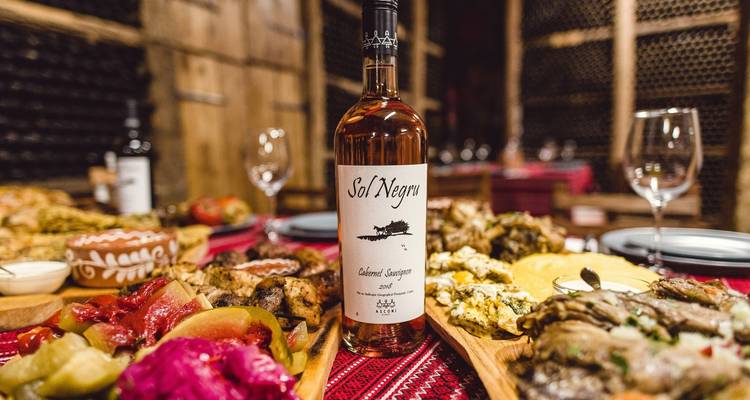 Tafel met verschillende heerlijke gerechten en een fles wijn getiteld Sol Negru.