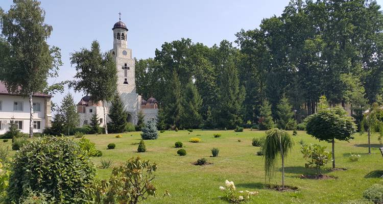 Église blanche avec jardins et arbres autour.