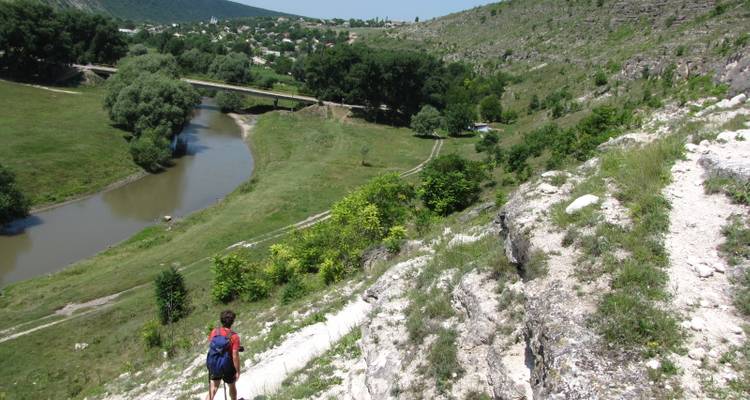 Vue large d'une vallée verte avec une rivière et un randonneur.