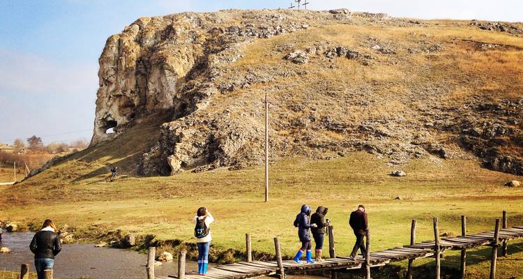 Des gens traversant un pont en bois près d'une colline rocheuse.