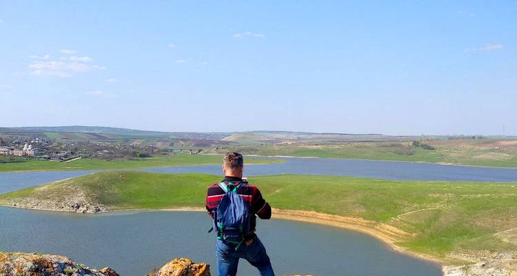 Man standing on a hill overlooking a wide landscape of rivers and fields.