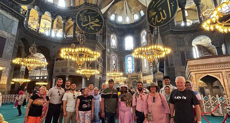Un grand groupe de touristes pose sous les lustres dorés à l'intérieur de la Sainte-Sophie d'Istanbul.