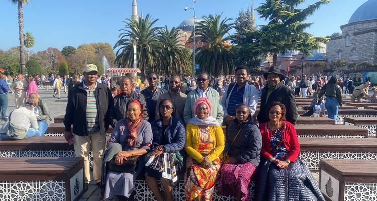 Groupe assis sur des bancs en bois dans une place animée avec des palmiers et les dômes de Sainte-Sophie en arrière-plan.