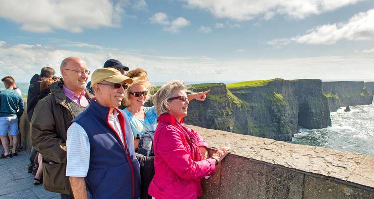 Des touristes âgés souriants pointant du doigt les spectaculaires Falaises de Moher depuis une terrasse d'observation