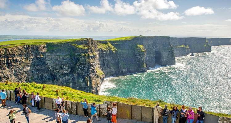 Vue panoramique large des Falaises de Moher avec des visiteurs le long de la bordure herbeuse et l'Atlantique turquoise en dessous