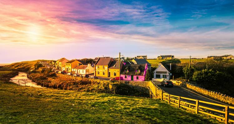 Village côtier irlandais coloré baigné dans la lumière chaude du coucher de soleil avec la campagne vallonnée environnante