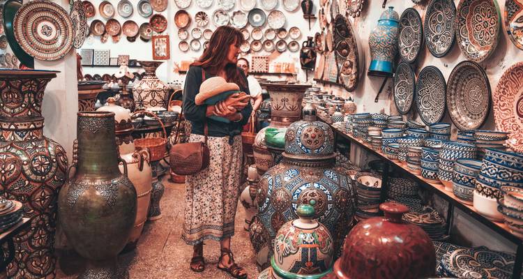 Woman shopping in a traditional market with shelves full of colorful pottery and ceramics.