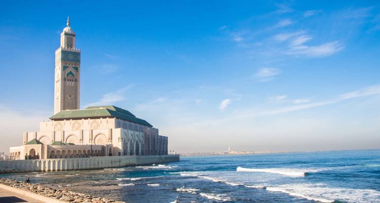 View of the Hassan II Mosque by the sea with clear blue skies.