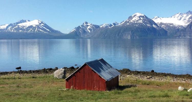 Wooden cabin by a tranquil lake with snow-capped mountains.