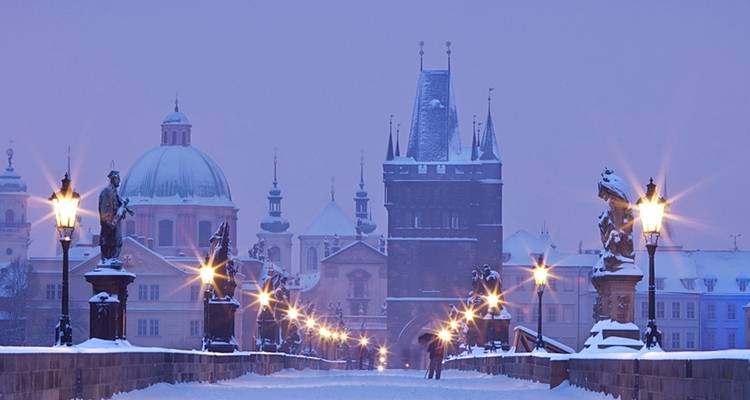 Puente de Carlos cubierto de nieve con estatuas y paisaje urbano al fondo.