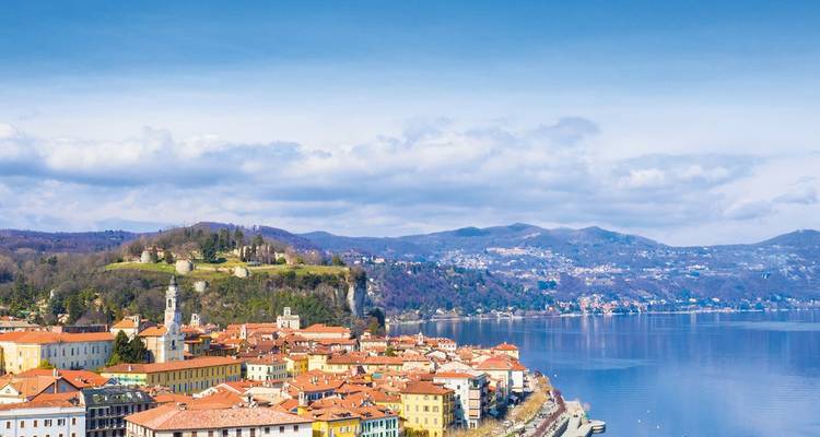 Colorful lakeside Italian town with red roofs lining the calm blue waters of Lake Maggiore.