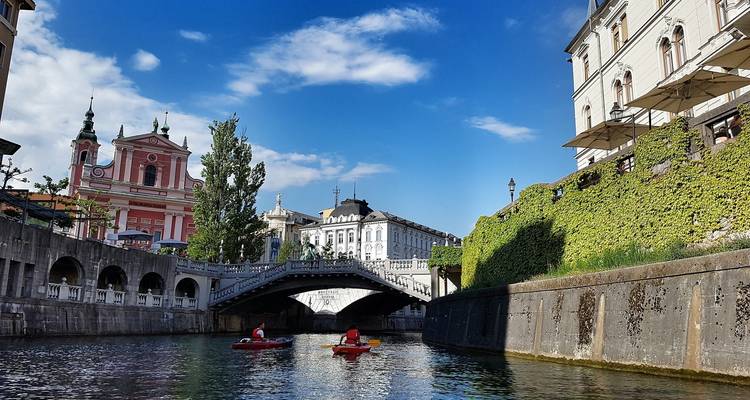 Scenic canal in Ljubljana with kayakers and colorful buildings.