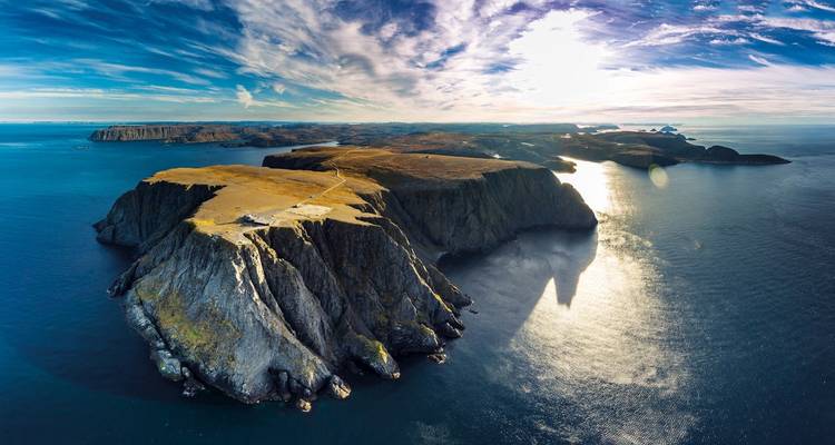 Vista aérea de acantilados dramáticos y el océano, con la luz del sol reflejándose en el agua.
