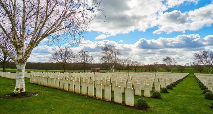 Reihen von weißen Grabsteinen auf einem Friedhof unter bewölktem Himmel.