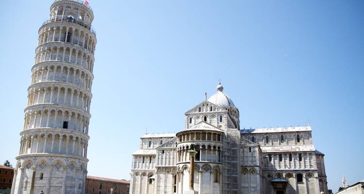 Scheve toren naast een kathedraal onder een heldere hemel.