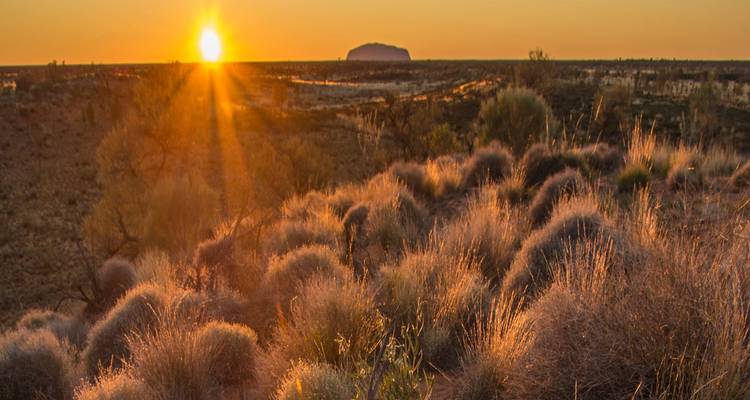 Coucher de soleil sur un paysage désertique avec une formation rocheuse proéminente au loin.