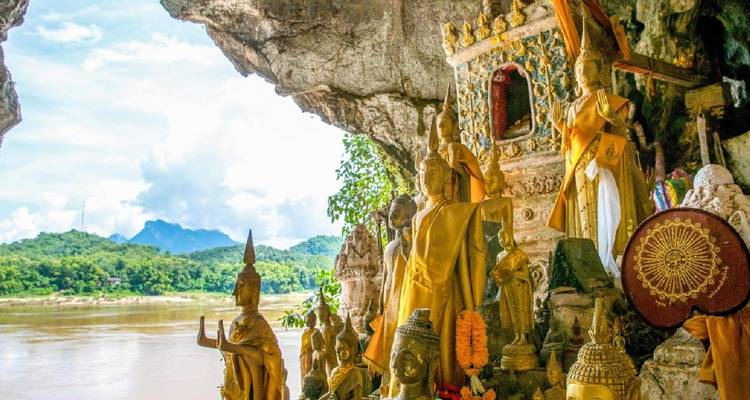 Statues bouddhistes dans une grotte surplombant une rivière.