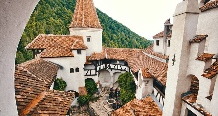 Uitzicht op de binnenplaats van Bran Castle met witte muren, dakpannen en beboste heuvels daarachter.
