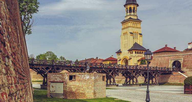 Houten brug en gele klokkentoren binnen het Alba Iulia Citadelcomplex op een zonnige dag.