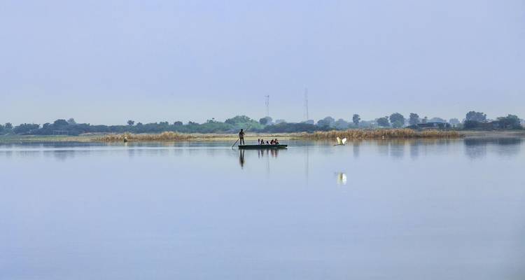 Kleines Boot auf ruhigem Wasser mit Menschen, umgeben von Schilf.