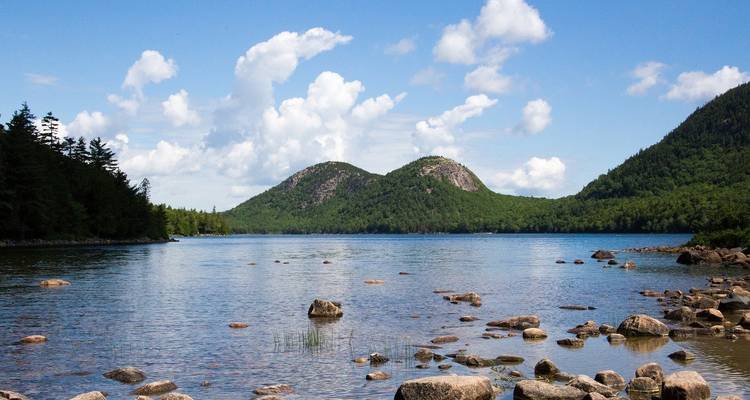 Ein ruhiger See, umgeben von Grün und Hügeln.